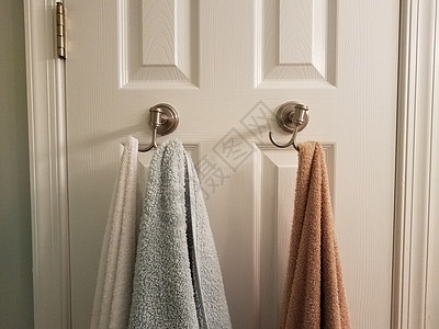挂在白色浴室门上钩子上的毛巾图片