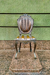 在绿墙背景下 在大理石展台的青铜椅子纪念碑上图片