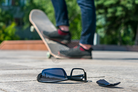 一个男人在滑板上滑冰的背景下 迷失的黑色眼镜就躺在路边图片