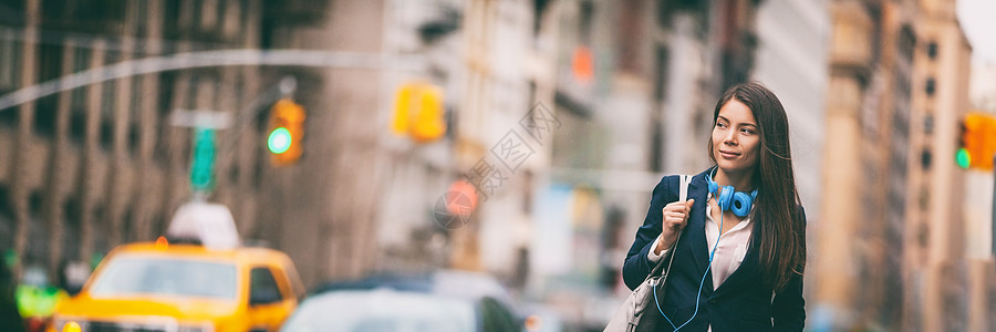 在纽约市街上行走的亚洲青年妇女 城市人口时装女郎在交通横幅全景条旗下 与钱包和耳机并肩搭靠边通勤的中国女士背景图片