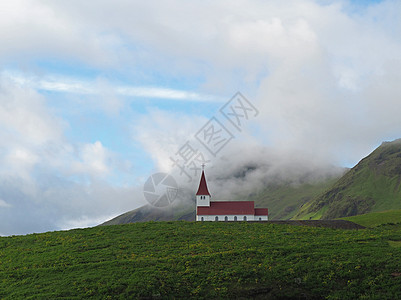 孤单的红白色教堂 在冰地绿草山和低云中背景