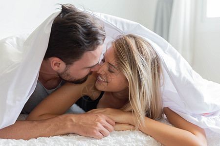 一对在床上的情侣看着相机 与快乐的爱人微笑幸福男生男朋友胡须拥抱男性卧室说谎妻子眼睛图片