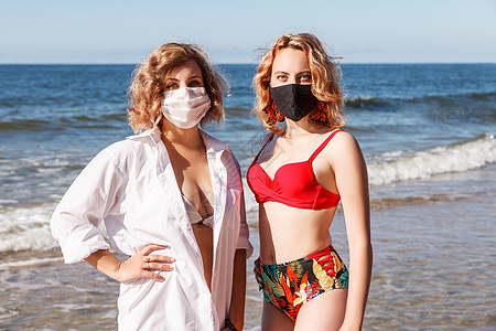 两个金发女孩穿着泳衣和防伪面具 身穿泳装的年轻金发女孩晴天女孩们安全比基尼身体预防蓝色海滩感染金发女郎图片