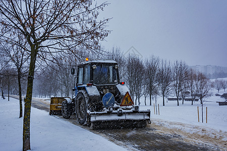 拖拉机在下雪时从人行道上扫雪背景图片