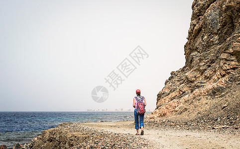 带着背包的红色红帽年轻女游客沿着R女士旅行冲浪地平线海岸闲暇山路石头小路休息图片