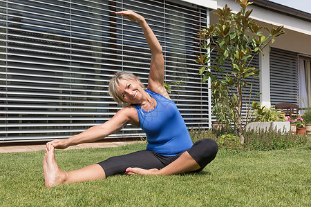 柔软的金发老金发女郎在户外锻炼姿势训练灵活性公园植物花园教练先行者私人运动装图片