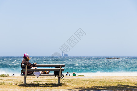 坎普斯湾的风沙滩上坐着长椅的女人图片