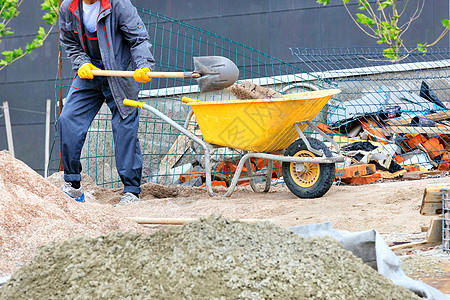 工人用铲子把沙子装进一辆黄色的建筑手推车图片