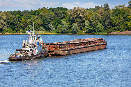 一艘载有空生锈驳船的拖船横渡一条宽阔的河流图片