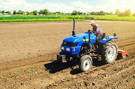 拖拉磨蹭农民在拖拉机上用铣床加工松散农田的土壤 在种植园中研磨和混合土壤 准备新作物种植 疏松地表 耕种土地背景
