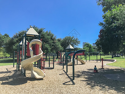 儿童游乐在美国得克萨斯州达拉斯市中心公园公共公园游乐场上玩耍的不明身份的小孩亚裔男孩 周围被大树包围城市孩子娱乐塑料邻里树木运动天际建筑背景