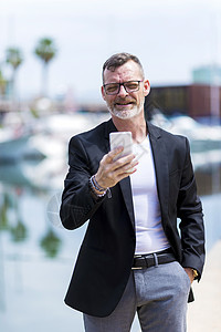 成熟商务人士在户外与港口对峙时使用手机的手势成人细胞消息互联网电话夹克眼镜胡子银行业经纪人图片