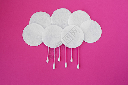 粉红色棉芽上方有白头和白色圆形棉花盘 在粉红色背景的雨滴下云中铺放图片