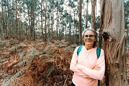 坐在树上 微笑着笑着在森林里拍镜头的老女人 穿着运动服女性头发倾斜享受时间乐趣退休女士老年相机图片