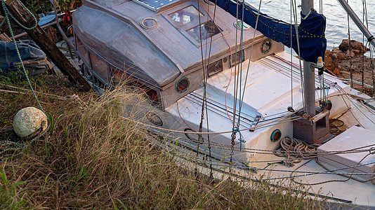 一艘废弃在失修状态中的旧木船在红树林河岸上停靠 被废弃的老木船破损不堪图片