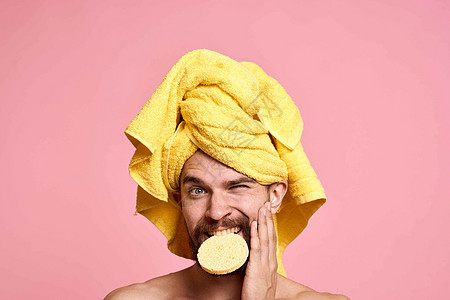 海绵头上有黄毛巾的男人 干净的皮肤护理粉红色背景治疗身体眼睛奶油成人男生微笑浴室卫生温泉图片