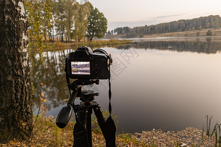 三脚架上的黑色数码相机 以有选择性的焦点拍摄秋湖早雾明晨风景日落单反摄影相机薄雾照片桦木爱好树木镜片图片
