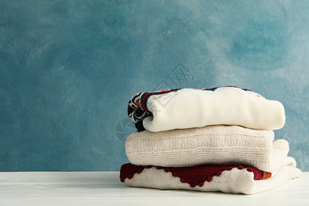 蓝色背景的白色木制桌子上毛衣垫子折叠服装木头织物收藏套衫球衣羊绒衣服羊毛图片