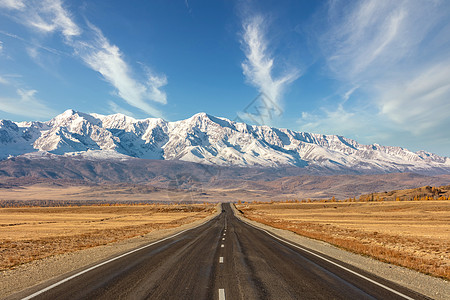 沙漠山通往 Kuray 山脉雪峰的一条笔直的空旷高速公路的镜头 美丽的蓝色多云天空作为背景 阿尔泰山脉 西伯利亚 俄罗斯背景