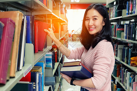 在图书馆里从书架上捡书的年轻女人学习图书女性大学知识女孩闲暇学校青少年白色图片