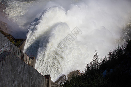 俄罗斯马加丹地区的科雷马水电站 从水力发电站的大坝溢洪道 一条巨大的水流在高山的背景下流入河流车站海浪技术水库涡轮薄雾镜头阳光蓝图片