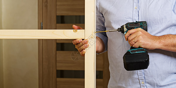 一名男子用自攻螺钉固定两根木梁 木匠用螺丝刀把螺丝包起来 石膏板木框架的构造维修修理工建设者木材建造椽子职业木板家具建筑背景图片