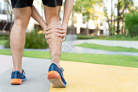 男性运动员腿部受伤和疼痛 手抓着痛苦的腿在公园里跑来跑去膝盖赛跑者女士跑步踪迹十字形治疗训练慢跑者小牛图片