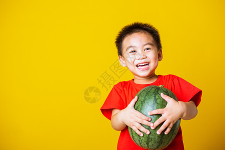 快乐的肖像亚洲儿童或可爱的小男孩穿着红色 T 恤玩耍时迷人的微笑拿着没有被切开的完整西瓜童年小吃男人营养蔬菜食物工作室喜悦假期饮图片