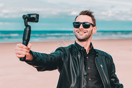 相机太阳镜帅哥在海滩自以为是照片快乐博客视频旅行博主旅游太阳镜皮夹克蓝色背景