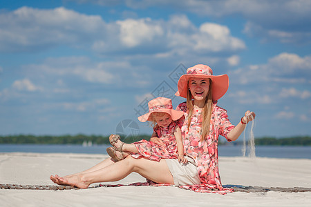 有个小女孩和她妈妈 在海滩沙滩上玩的漂亮晒太阳衣 时髦的家庭风貌 笑声情感拥抱帽子母亲裙子母性孩子女性女士幸福图片