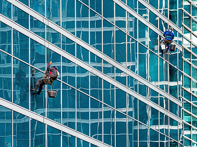两个带有安全系绳的工业登山者洗刷现代摩天大楼的玻璃墙 在大都会从事危险工作城市建筑学工人绳索建筑蓝色电缆高度办公室玻璃图片