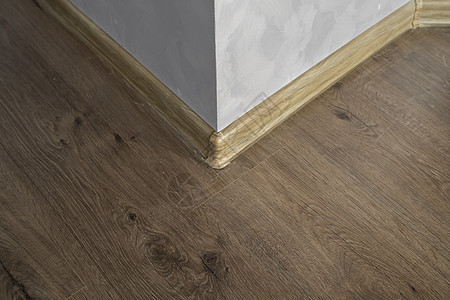与具有木质纹理的塑料底板层压 家里新安装的强化木地板和踢脚板 现代设计 深色橡木地板镶木地板上塑料底座的特写风格角落控制板建筑学图片