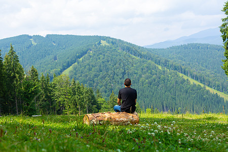 坐在原木上并享受和平的绿色山地景色的人 思想平静和放松自由岩石男性爬坡天空远足背包森林冒险悬崖图片
