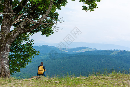 一个人坐在悬崖上享受和平的绿色山地景色 心平气和 放松远足者冒险假期游客岩石运动自由石头背包森林图片