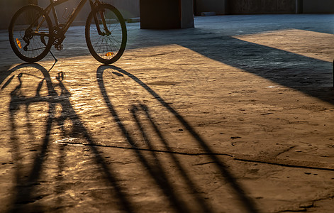 黄色的傍晚阳光穿过停车场的山地自行车车轮城市车道运输阴影车辆框架建筑闲暇水泥齿轮图片