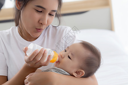 年轻的亚洲母亲在家里用奶瓶拥抱和喂养小女婴 新生儿的纯真与妈妈满意地喝酒 妈妈和孩子的关系和结合 家庭观念新生女性童年母性房间牛图片