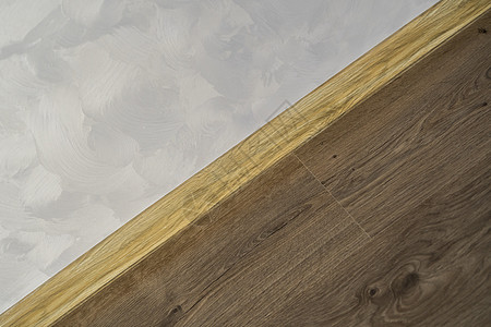 与具有木质纹理的塑料底板层压 家里新安装的强化木地板和踢脚板 现代设计 深色橡木地板镶木地板上塑料底座的特写建筑材料木板装饰建筑图片