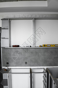 没有家具立面 mdf 的定制厨柜安装 灰色模块化厨房由刨花板材料制成 在厨房的不同安装阶段 地板和墙壁上铺有灰色瓷砖家庭家居贮存背景图片