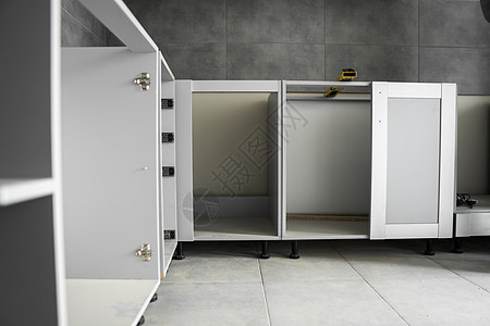 没有家具立面 mdf 的定制厨柜安装 灰色模块化厨房由刨花板材料制成 在厨房的不同安装阶段 地板和墙壁上铺有灰色瓷砖维修服务橱柜背景图片