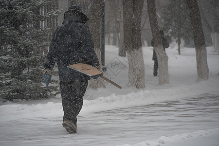 市政服务的一名工作人员带着雪铲在暴风雨 暴风雪或冬季降雪中在城市的恶劣天气中沿着道路行走 北方的极端冬季天气条件温度设备冰川气旋图片