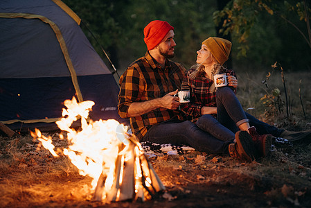 一对年轻夫妇 一个男人和一个女孩 戴着漂亮的编织帽子 在露营时停下来了金发女郎胡须帐篷女孩旅行天空橙子篝火蓝色数字图片