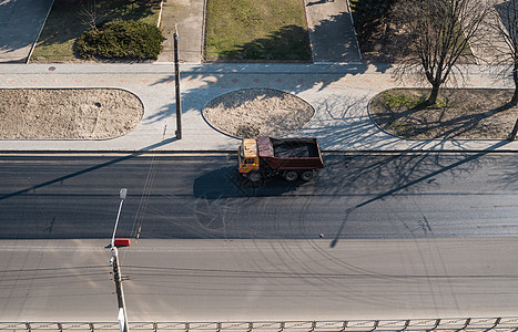 在道路建设工程期间 一辆卡车在城市的一条公路上开着破碎石倾倒工作露天船运石头司机机械车身机器搬运工图片