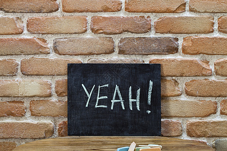 粉笔板上写着“YA”字! 用手和粉笔淹死在砖墙背景的木制桌子上图片