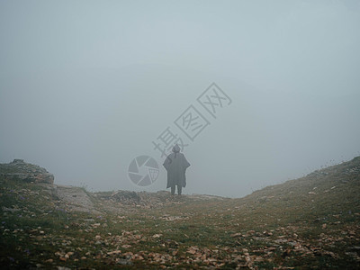一个穿黑大衣和兜帽的男人在山上行走图片
