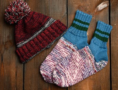 一对温暖舒适的编织袜子 和一顶棕色木头背景的毛帽图片