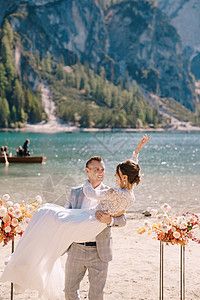 在意大利的背景下 新郎在婚礼场地将新娘抱在怀里 用两个秋天的花柱代替拱门 婚礼在欧洲 在 Braies 湖上分支机构新婚橙子捧花图片