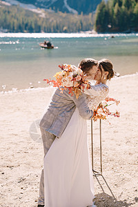 新婚夫妇在意大利布拉埃斯湖的背景下 以秋天的花柱拱门为仪式现场亲吻 在欧洲的目的地婚礼 在 Braies 湖上干花树叶岩石夫妻衬图片