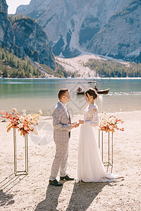 新郎在婚礼场地为新娘戴上戒指 在意大利的背景下 以秋季花柱拱形为背景 欧洲的目的地婚礼 在 Braies 湖夫妻玫瑰新婚岩石山脉图片