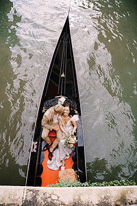 意大利威尼斯婚礼 一位船夫载着新娘和新郎乘坐经典的木制贡多拉沿着狭窄的威尼斯运河行驶 在古建筑的背景下 新婚夫妇坐在船上合伙街道图片