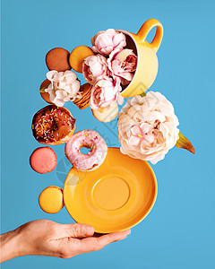 黄杯 甜甜圈 马卡龙 小马和手持纸碟中的松饼生命 在蓝色背景上飞翔图片
